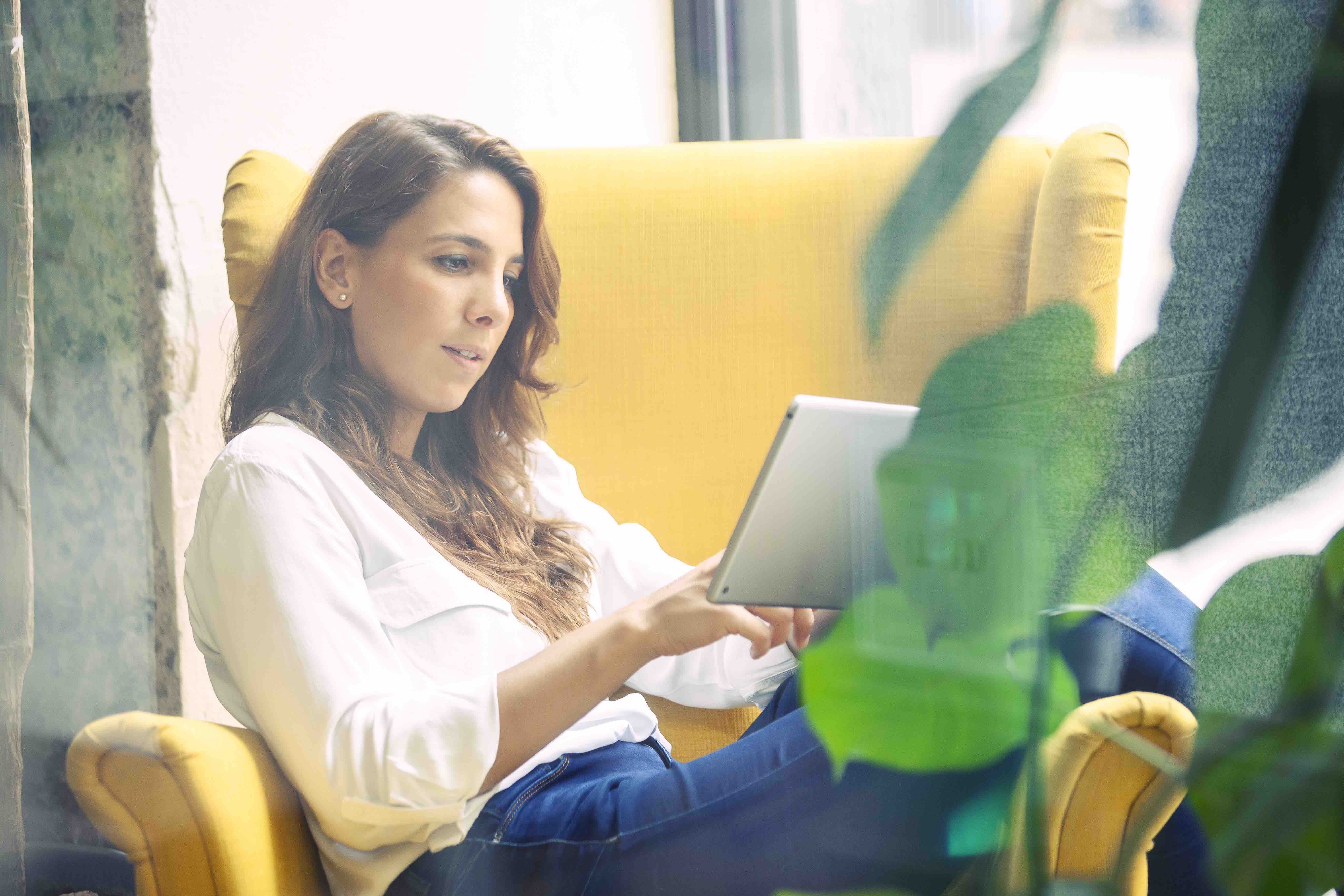 Young woman reading a book in a tablet device sitting in a yellow coach.