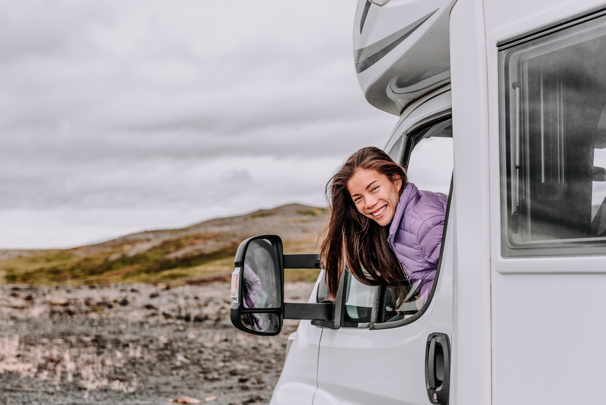 RV camper trailer travel woman driving motorhome camping van on Iceland road trip. Asian tourist driver smiling peeking out window of front seat