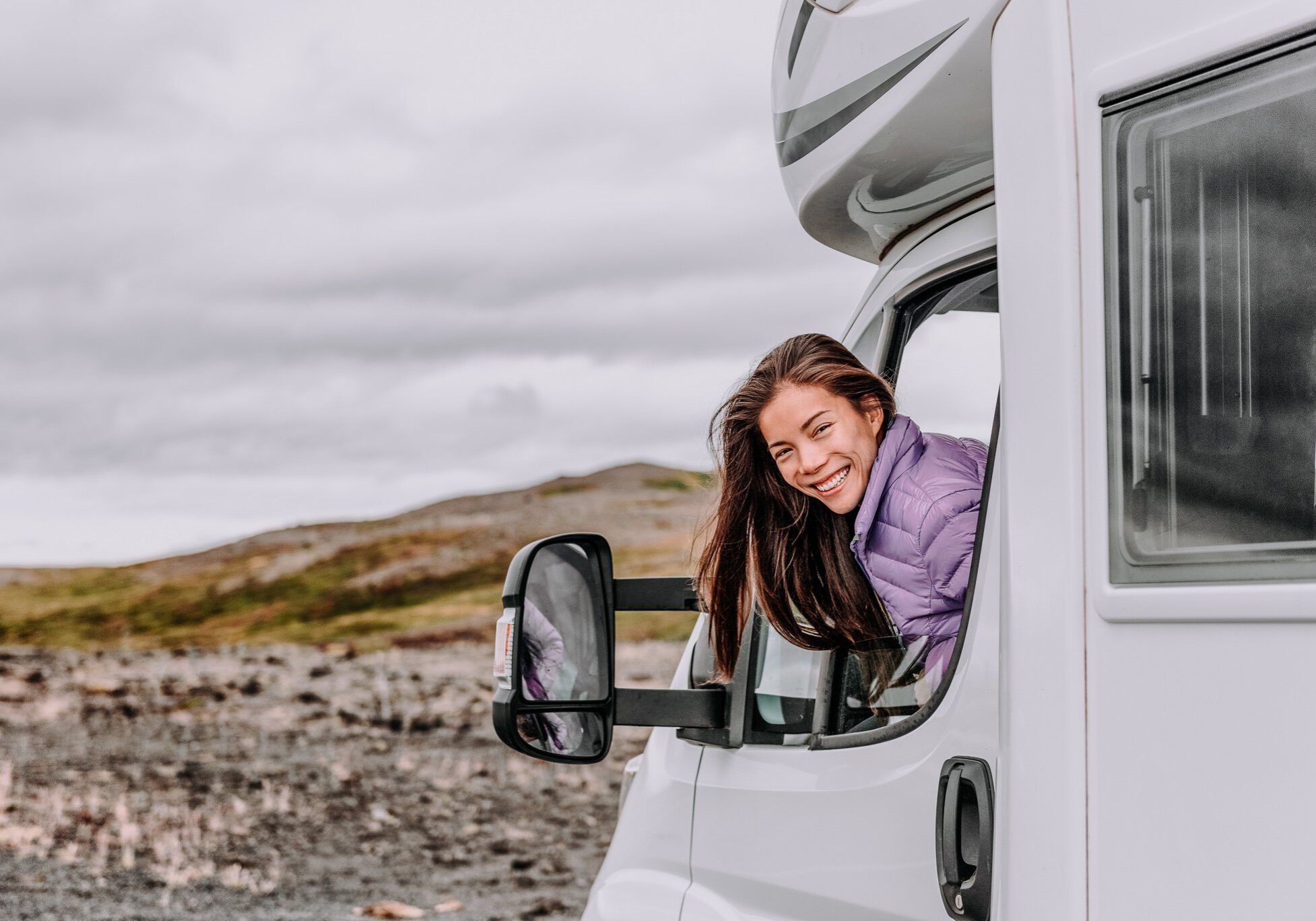 RV camper trailer travel woman driving motorhome camping van on Iceland road trip. Asian tourist driver smiling peeking out window of front seat
